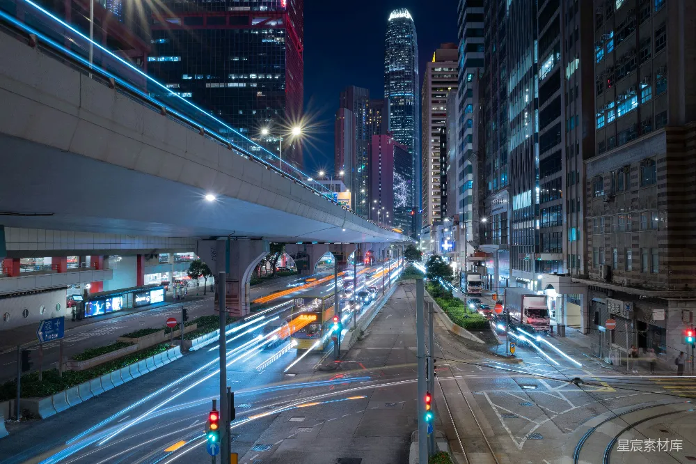 这张图片展示了香港繁忙街道的夜景。画面中高楼大厦林立，灯光璀璨，形成了独特的视觉效果。街道上车辆的光轨和路标清晰可见，体现出城市的活力与繁忙。适合用于表现城市夜景、都市生活或现代都市的繁华景象。