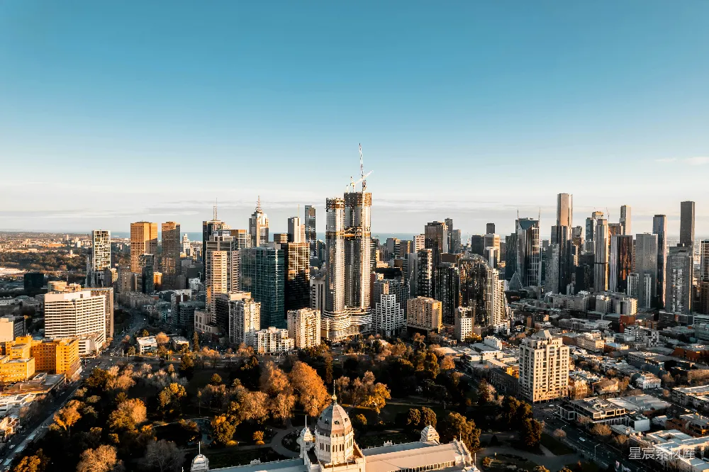 这张图片展示了清晨时分，现代都市的天际线。高楼大厦错落有致，建筑风格现代，阳光从右侧照射而来，给城市带来温暖的色调。前景中可以看到一些树木和公园，为城市增添了一丝自然的气息。整体画面给人一种宁静而充满活力的感觉。