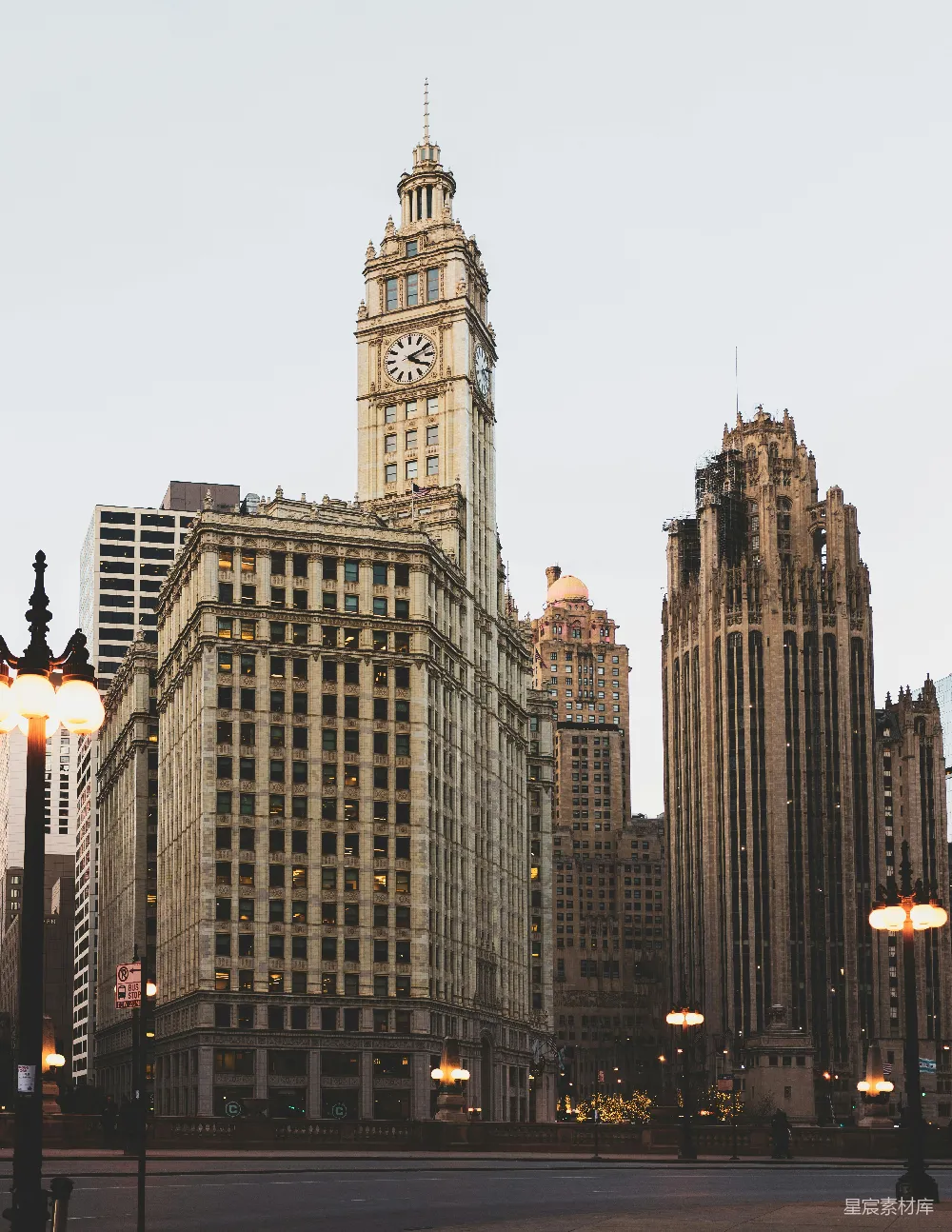 这张图片展示了芝加哥的标志性摩天大楼，其中包括著名的Wrigley Building，其独特的钟楼和华丽的建筑风格，展现了城市的历史与优雅。画面中的灯光和建筑物在黄昏时分显得格外温暖，营造出一种宁静而充满故事感的氛围。