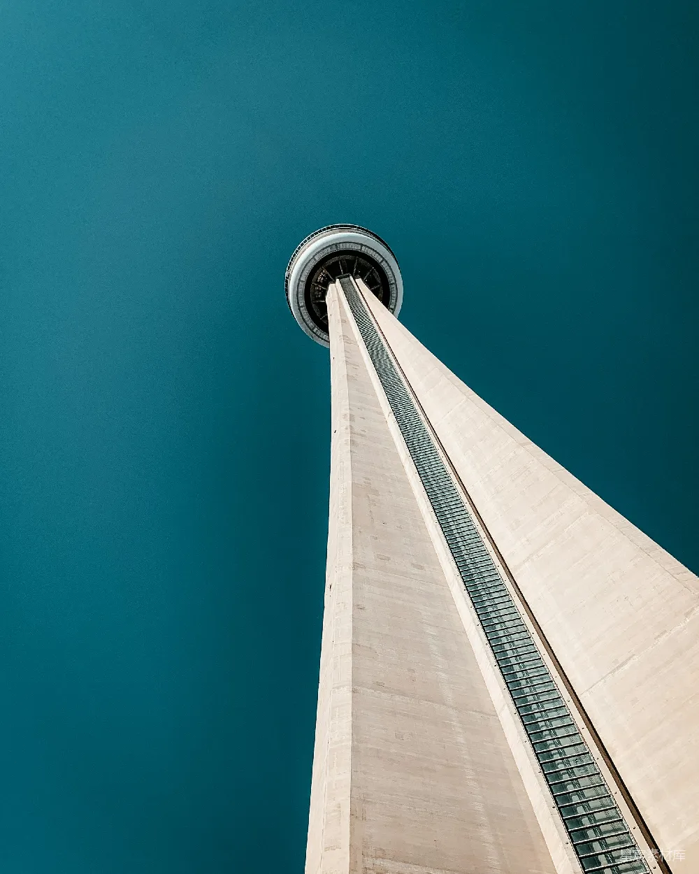 这张图片展示了加拿大国家电视塔（CN Tower）从低角度仰视的景象。天空呈现出深邃的蓝色，与白色塔身形成鲜明对比，展示了建筑的宏伟与城市的天际线。这种视角常用于展现建筑的高耸与现代感，适合城市风光、建筑摄影爱好者以及旅游相关的素材使用。