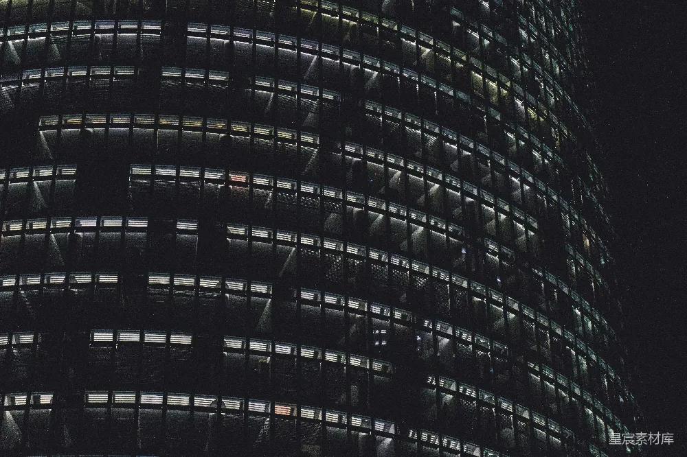 这张图片展示了夜晚一座摩天大楼的景象。建筑的玻璃幕墙在黑暗中反射着微弱的光亮，形成了许多条光线，营造出一种神秘而又静谧的氛围。这样的场景通常出现在现代都市的夜景中，适合用于表现城市生活的繁忙与静谧，或是用于商业、科技或都市生活的相关主题。