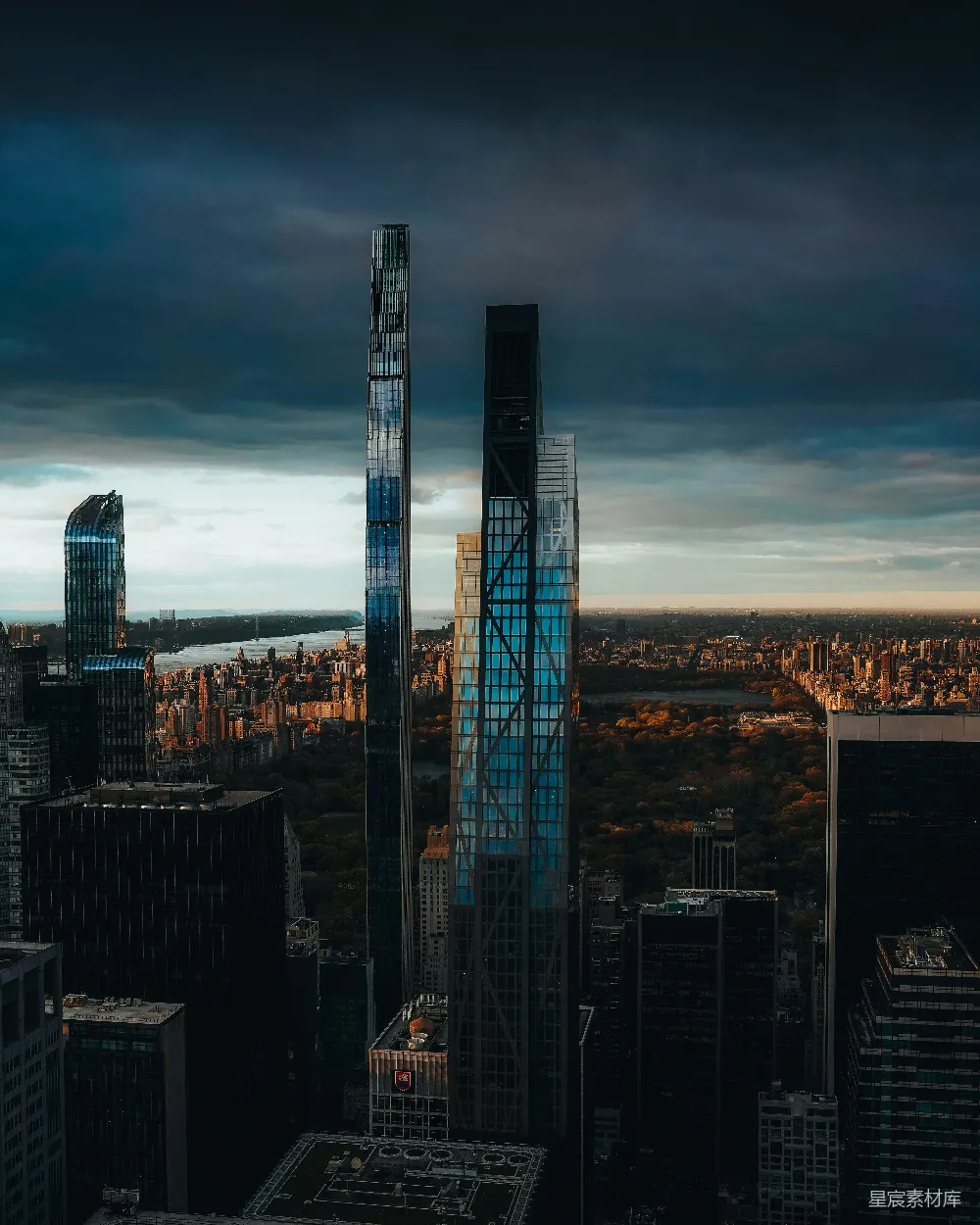 这张图片展示了纽约市曼哈顿摩天大楼与中央公园的日落景象。高耸的玻璃幕墙建筑在夕阳的映照下显得格外醒目，而公园中的树木在余晖中展现出柔和的轮廓。整个场景充满了现代与自然的对比，展现了城市与自然和谐共存的美丽。