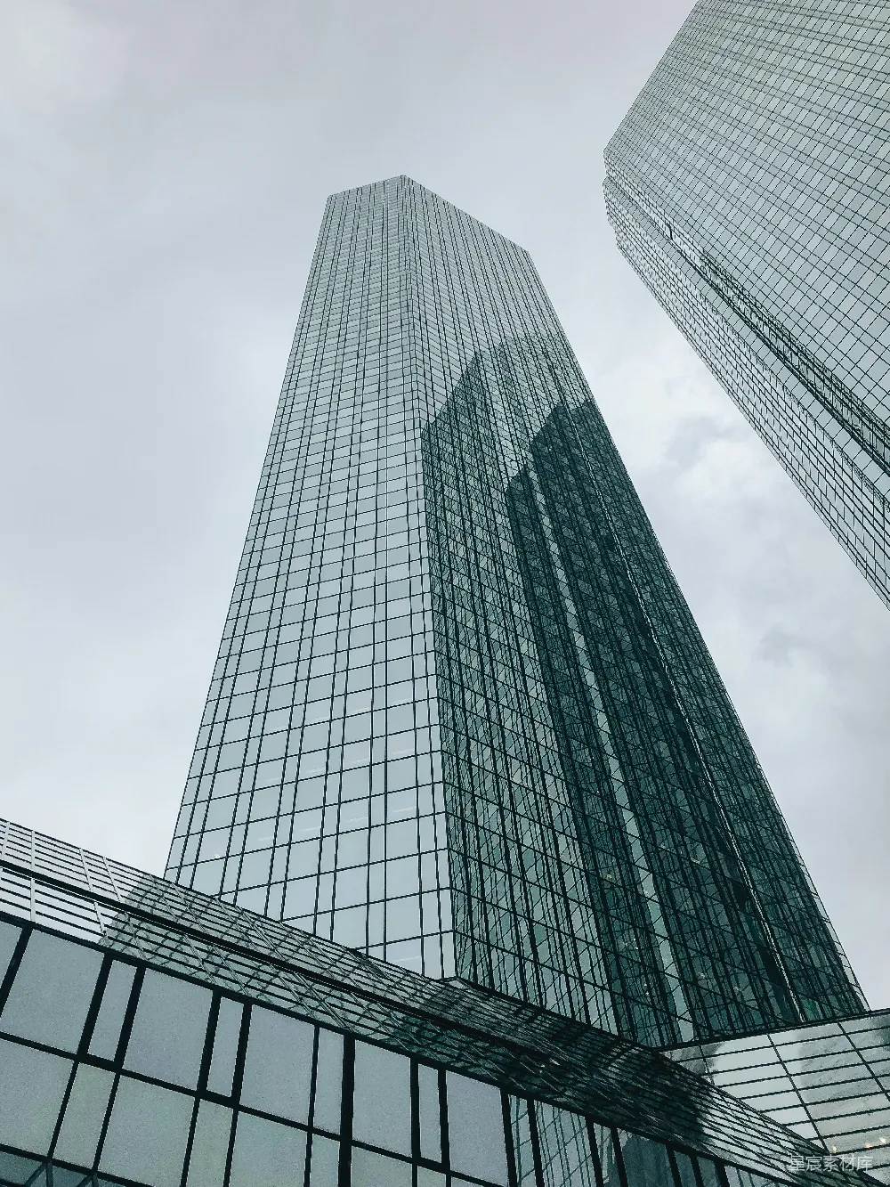 这张图片展示了两栋高耸入云的摩天大楼，其玻璃幕墙反射出天空的色调，形成了独特的视觉效果。建筑物的线条简洁而有力，体现了现代建筑设计的简洁与宏大。适合用于都市建筑、现代建筑风格展示或城市风光的背景素材。