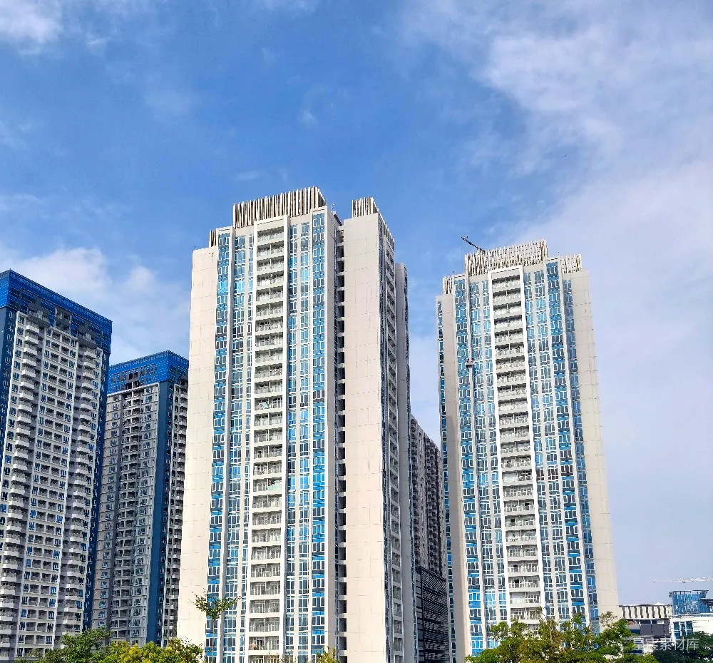 这张图片展示了现代化的高层建筑群，背景是蓝天白云，展示了城市的现代风貌。建筑的玻璃幕墙反射出蓝色的天空，给人一种清新、开阔的感觉。适合用作城市风光、建筑设计或现代生活场景的背景素材。