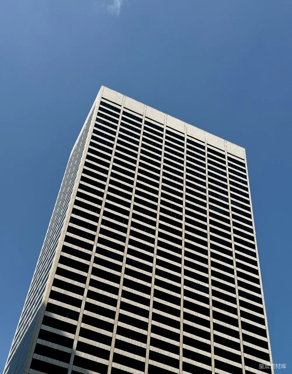 这张图片展示了从地面仰视摩天大楼的视角，展现了建筑的高耸与现代城市建筑的宏伟。画面中天空湛蓝，与建筑物的冷色调形成鲜明对比，突显了建筑的简洁线条和结构美感。适合用于城市景观、建筑美学或现代城市发展的展示。