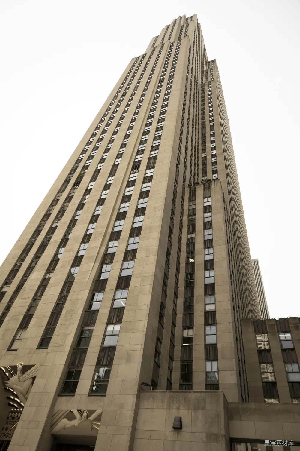 这张图片展示了一座高耸入云的摩天大楼，建筑风格复古，采用了大量的窗户设计。这座建筑是纽约著名的洛克菲勒中心的一部分，以其独特的建筑艺术和标志性的人物雕塑而闻名。适合用于城市景观、历史建筑或地标相关的主题展示。