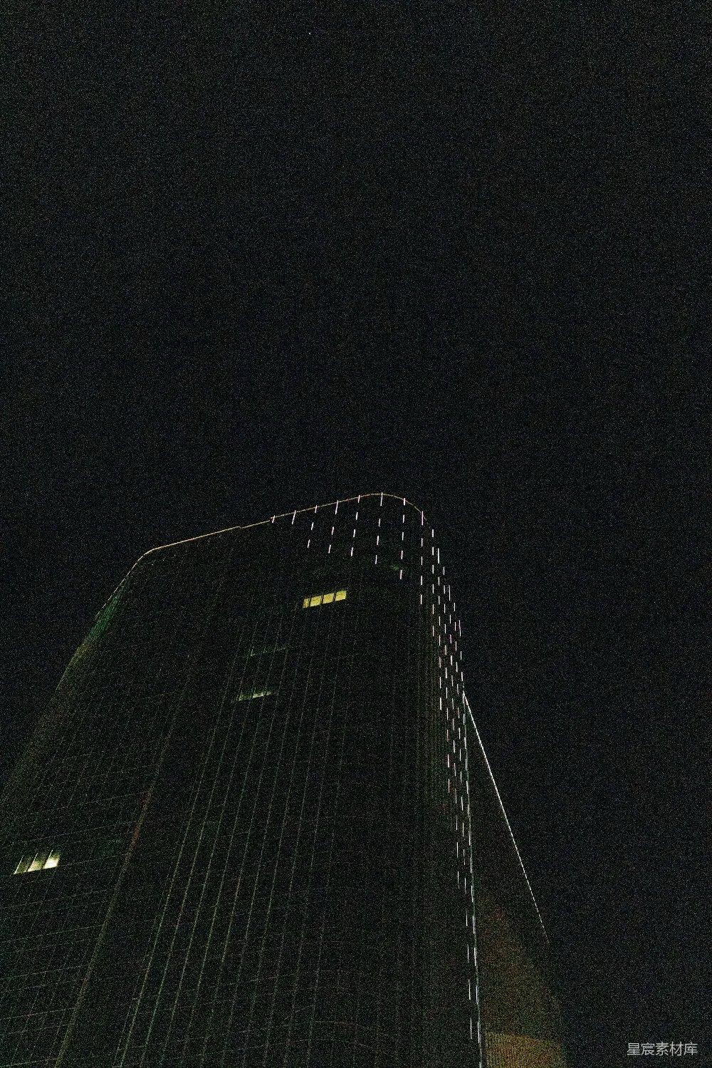这张图片展示了夜晚中的一座摩天大楼，在黑暗的背景下显得格外突出。大楼的灯光勾勒出其独特的轮廓，窗户中透出的微弱光芒增添了画面的立体感。适合用于表现现代都市的夜景、建筑美学或是城市生活的主题。