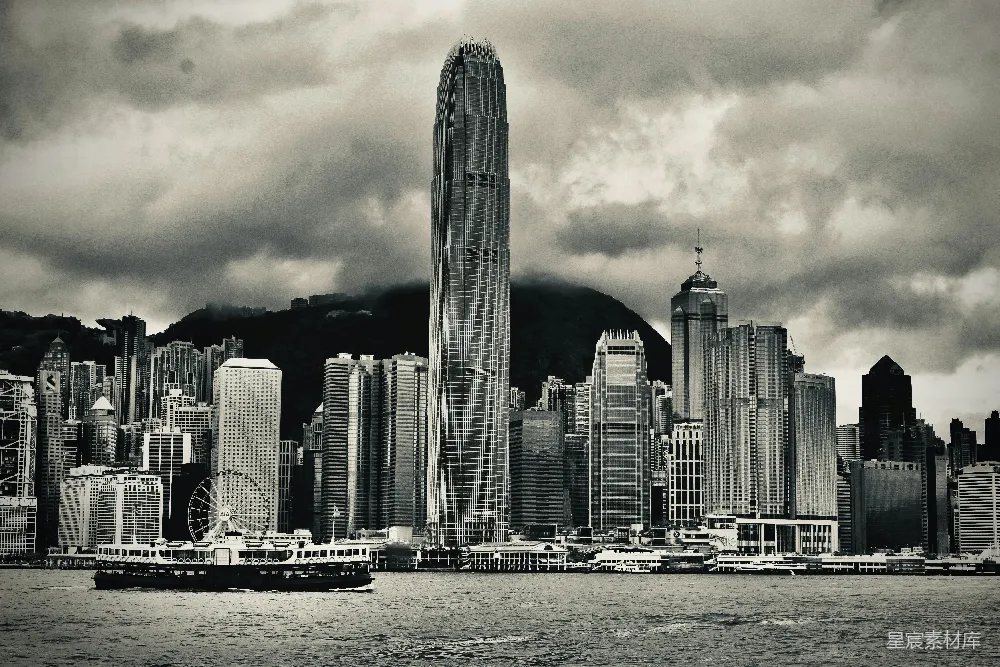 这张黑白照片展示了香港维多利亚港的天际线，中心是著名的国际金融中心大厦，背景是云层密布的天空和周围的高楼大厦。前景中，一艘游轮静静地停泊在水面上，为这幅城市风光增添了一份宁静。这张照片捕捉了香港现代化与自然环境交织的瞬间，展现了这座城市的独