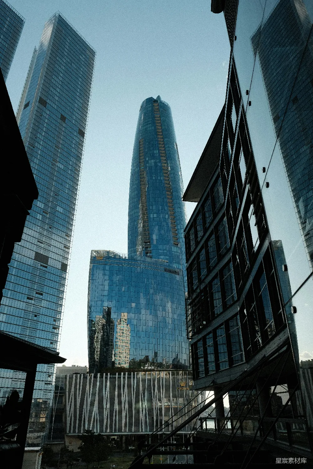 这张图片展示了现代城市中摩天大楼的壮观景象，建筑的玻璃幕墙在阳光下反射出周围建筑的倒影，形成了独特的视觉效果。天空清澈，光线充足，给人一种宁静而现代的感觉。适合用于展示城市景观、建筑设计或现代都市生活主题。