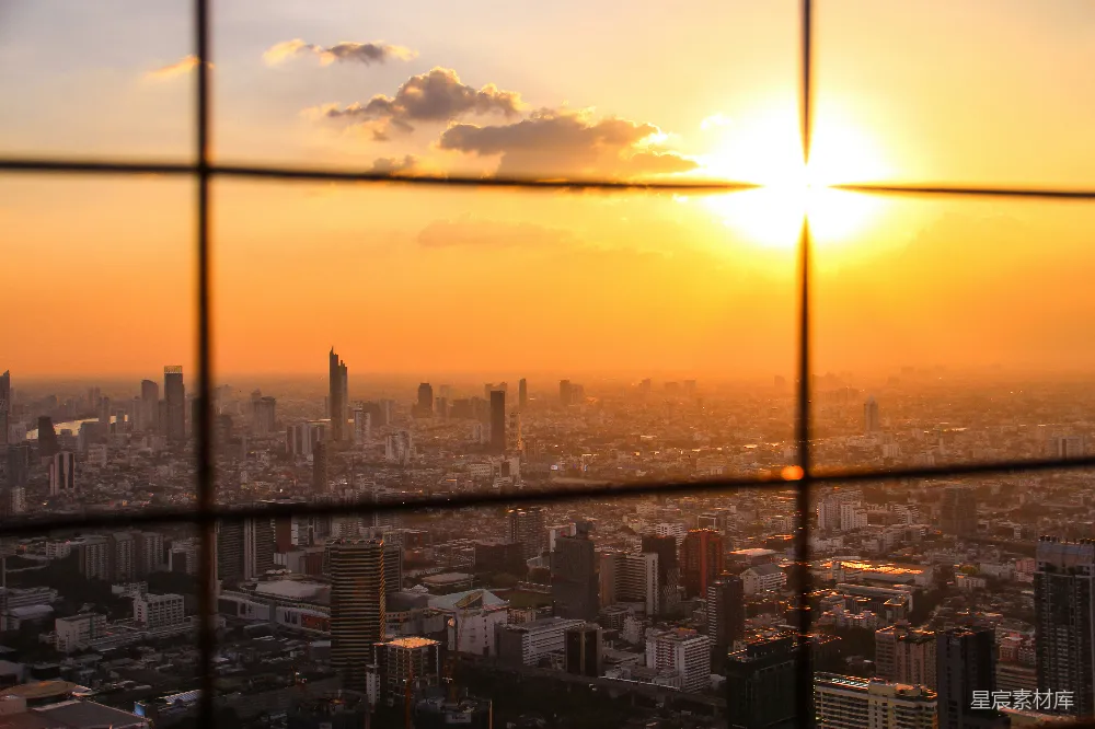 这张图片展示了城市黄昏时分的剪影，透过窗户的网格，夕阳的余晖洒在城市的天际线上，为高楼大厦披上了一层金色的外衣。天空中飘着几朵云彩，城市的轮廓在夕阳的映衬下显得格外壮观。这幅画面适合用于城市生活、自然风光、摄影艺术等场景。