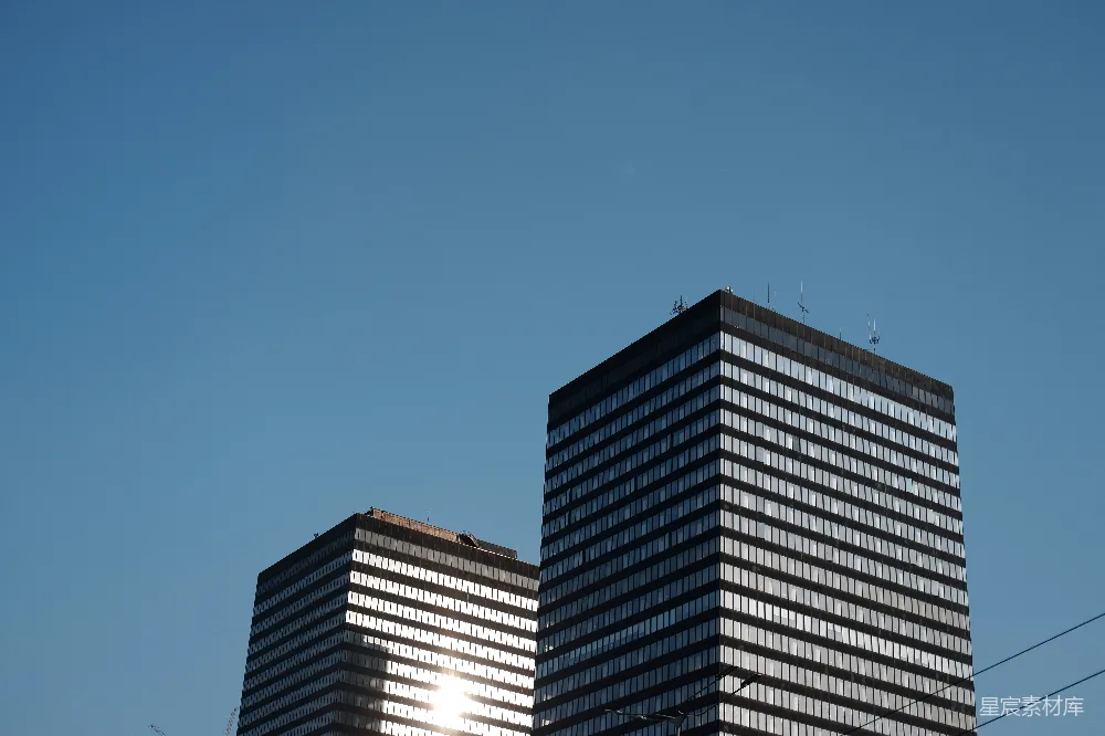 这张图片展示了两栋摩天大楼在蓝天下的景象。建筑物的玻璃外墙在阳光下反射出耀眼的光芒，给人一种现代都市的繁华与活力。背景是清澈的蓝天，没有云彩，显得格外宁静。适合用于城市风光、建筑美学或现代都市生活主题的场景。