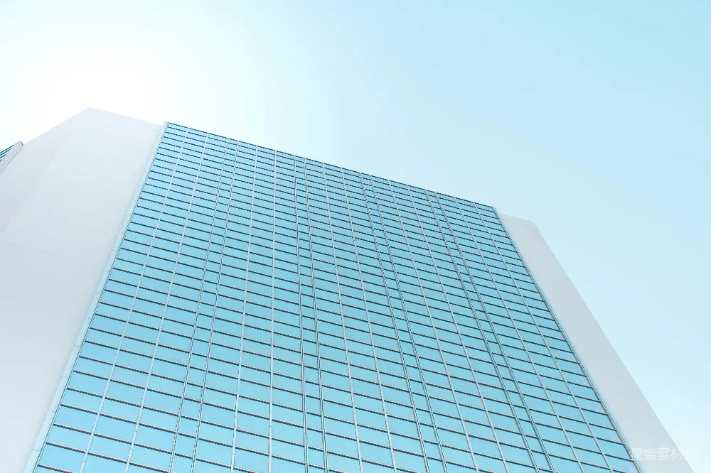 这张图片展示了一座现代化的玻璃幕墙建筑，其简洁的线条和大面积的玻璃反射出蓝天白云，给人一种开阔和未来感。适合用于现代城市、商务中心或城市风光的背景。