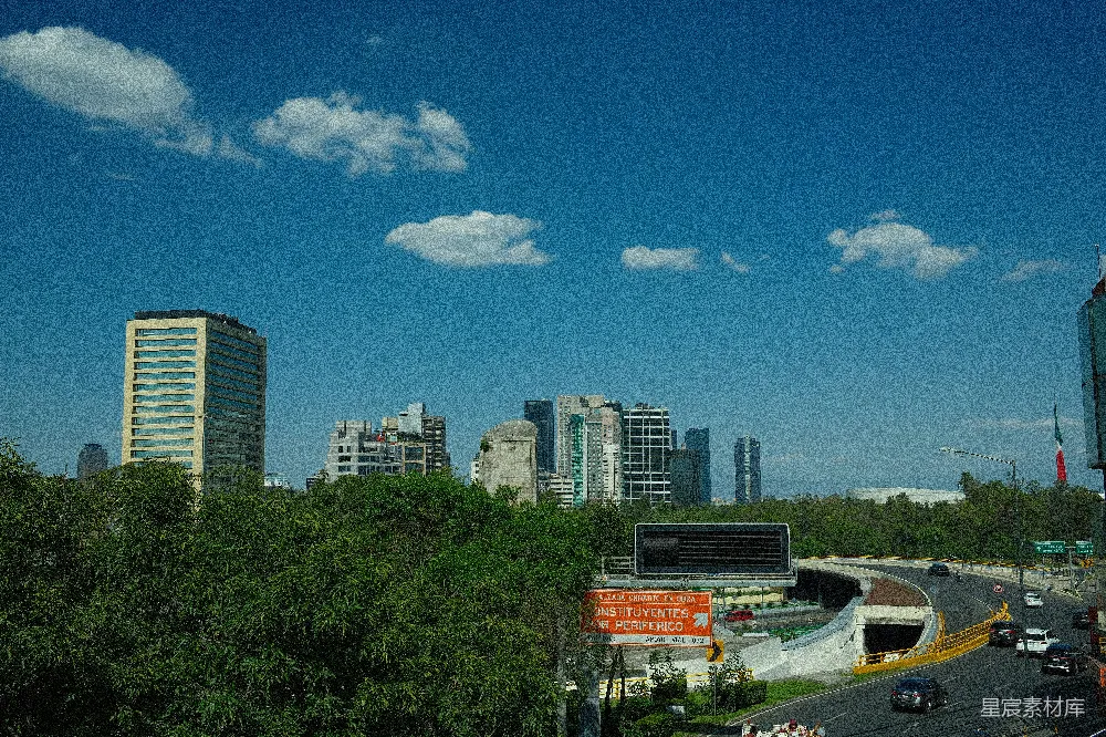 这张图片展示了晴朗天空下的城市景观，高楼大厦与绿树成荫的街道交相辉映，道路两旁车流不息，远处的建筑群与蓝天白云构成一幅和谐的都市画面。适合用于城市风光、建筑设计或交通主题的素材。