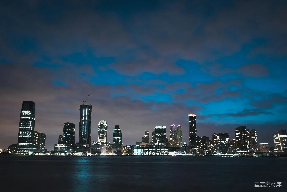 这张图片展示了一个城市的夜景，天空中云层点缀，城市中的高楼大厦灯火辉煌，反射在水面上形成美丽的倒影。这种场景适合用作城市夜景的封面图，或用于城市风光的宣传材料。