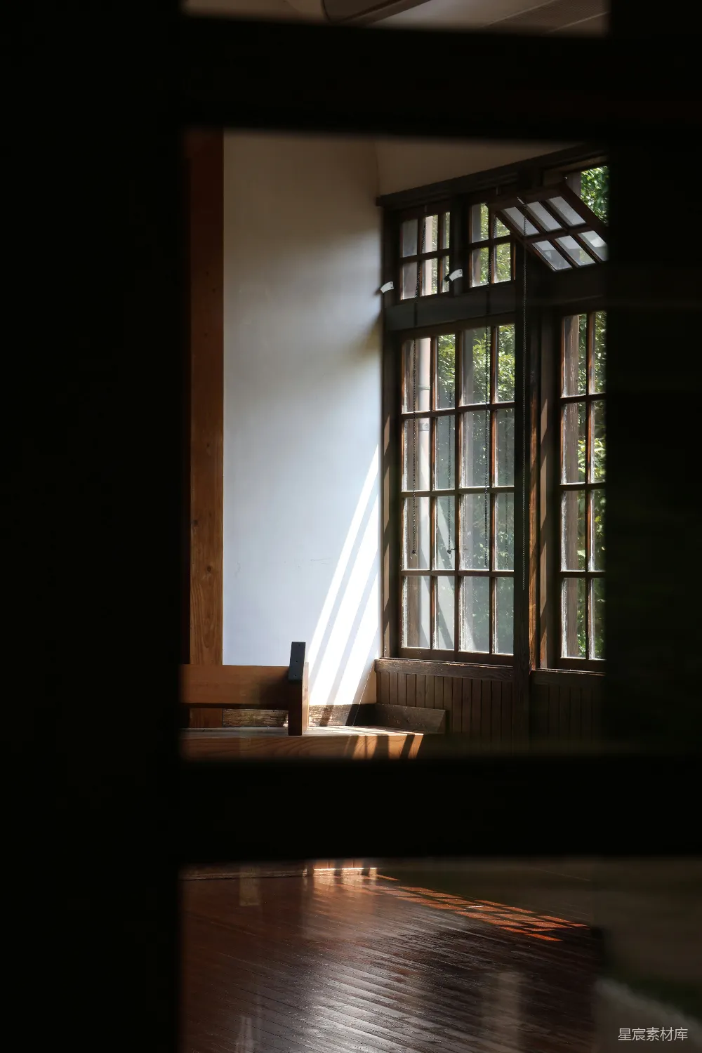 这张图片展示了一间室内场景，阳光透过窗户洒进房间，形成了美丽的光影效果。木质的地板和家具在阳光的照射下显得格外温暖和宁静。窗户的设计简洁而经典，窗外的绿色植物为整个场景增添了几分自然的气息。这种场景适合用于描述安静、温馨的室内环境，或者用于