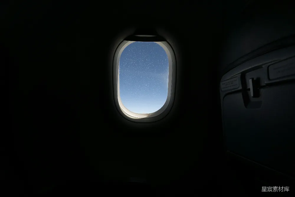 这张图片展示了从飞机窗户里拍摄的夜空，天空中布满了星星，显得宁静而美丽。背景是黑暗的机舱内部，窗户的光线透出窗外的夜空，营造出一种神秘而宁静的氛围。适合用于旅行、夜景和星空主题的图片。