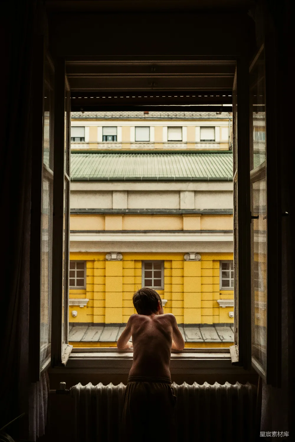 图片中，一个赤裸着上身的男孩站在窗边，凝视着窗外的黄色建筑。窗户的光线柔和，营造出一种温馨而怀旧的氛围。这个场景仿佛让人回到了童年的某个午后，充满着对未来的期待和对家的思念。