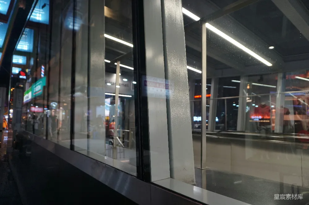 这张图片展示了夜晚城市中透过玻璃窗反射出的景象。玻璃窗上反射出街道上的灯光和店铺的招牌，营造出一种独特的城市夜景效果。玻璃窗的反光增添了画面的层次感，背景中隐约可见行人和店铺的标志，整个场景充满了现代都市的氛围。适合用于展示城市夜景、现代建