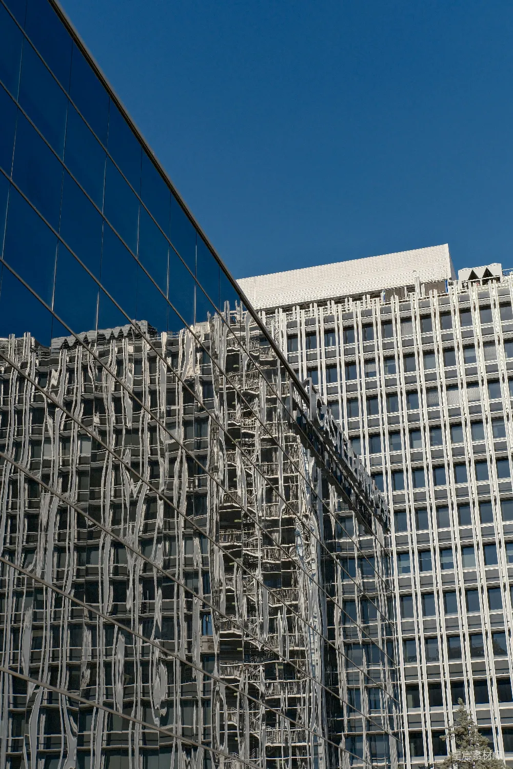 这张图片展示了现代城市的建筑景观，通过玻璃幕墙反射出另一座建筑的倒影，形成了一个有趣的视觉效果。画面中的建筑物线条清晰，结构简洁，展示了现代都市的建筑美学。背景是深蓝色的天空，使得整个画面显得更加高耸和宏伟。这种类型的图片适合用于城市风光、