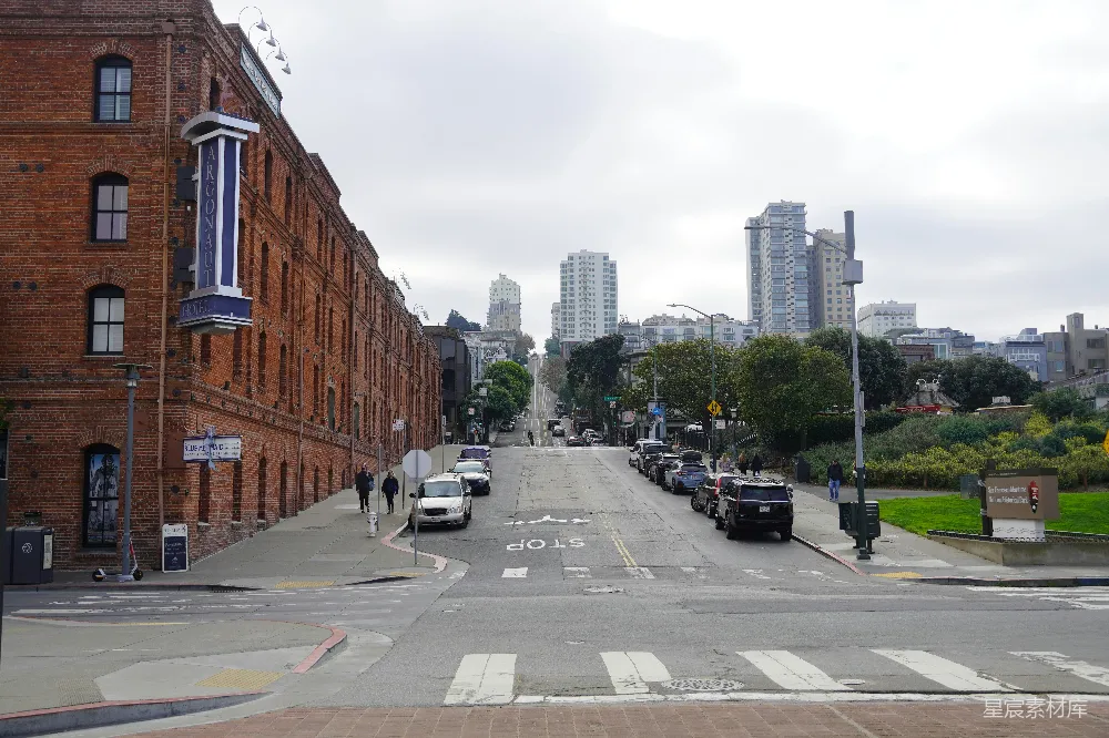 图片展示了一条宁静的旧金山街道，左侧是红砖历史建筑，右侧是现代化的高楼。街道两旁停着车辆，行人稀少，天空阴沉。这种场景适合用于介绍旧金山的城市风貌与历史保护区域。