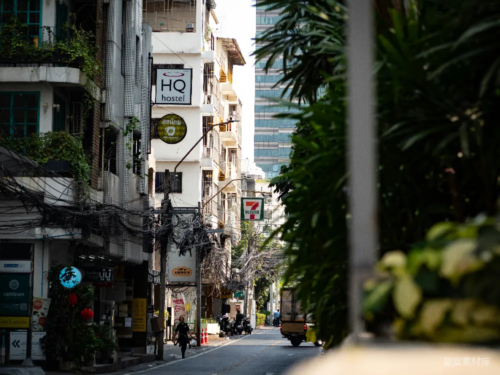 这张图片展示了城市的街景，街道两旁是老旧的建筑和现代的高楼，中间有绿植和一些店铺。街道上行人稀少，显得十分宁静。阳光透过树叶洒在路面上，给人一种宁静与和谐的感觉。适合用来展示城市生活中的另一面，或者作为城市风光的背景素材。