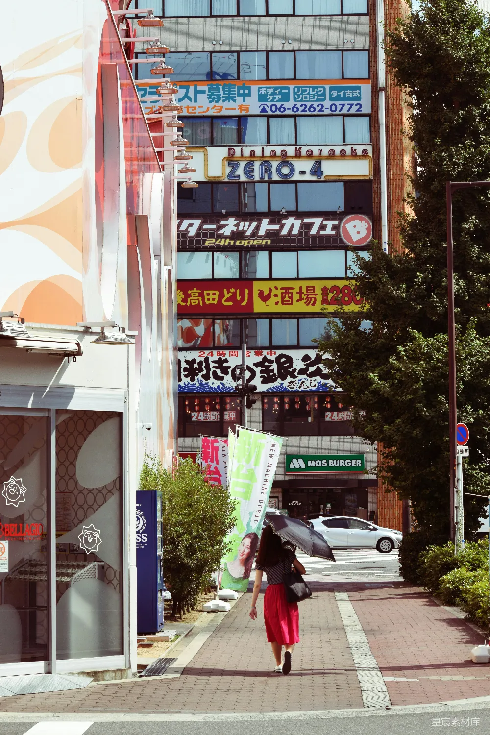 这张图片展示了一条充满活力的日本街道场景。前景中，一位女士穿着红色裙子，手持雨伞，悠闲地走在铺有红砖的小路上。背景是充满霓虹灯招牌的建筑，包括一个名为“Zero-4”的餐厅和一个MOS Burger快餐店。阳光明媚，树木郁郁葱葱，为城市景象