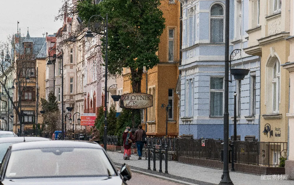 这张图片展示了欧洲某个小镇的街景，两旁是色彩丰富的建筑，街道上有行人和停放的汽车。整体氛围宁静而充满生活气息，适合展示欧洲小镇的日常生活和建筑风格。