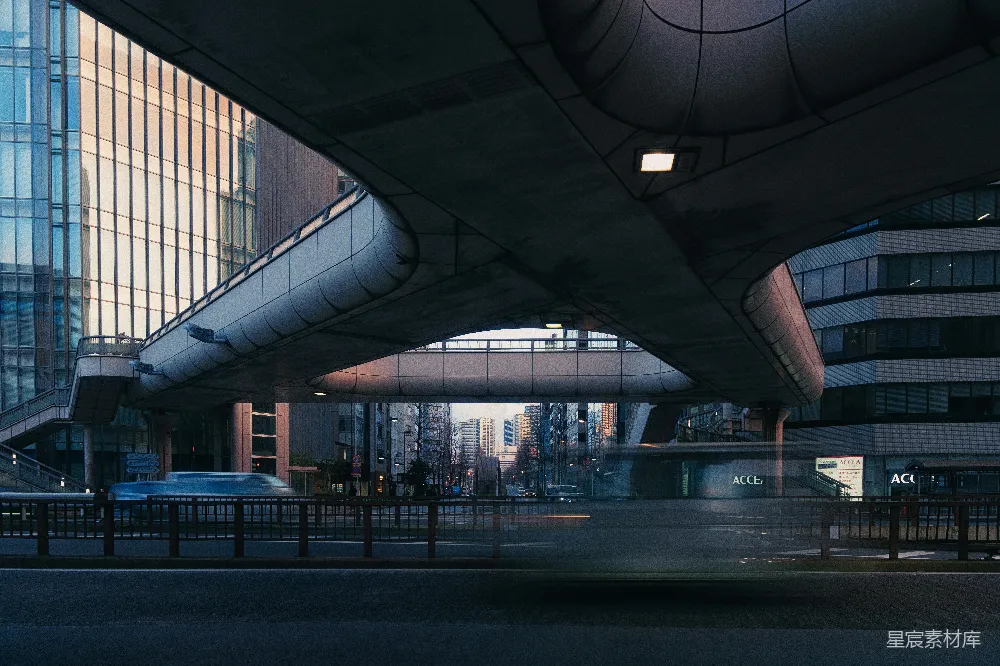 这张图片展示了一个城市的清晨，画面中有一座现代风格的建筑，其独特的拱形设计在清晨的阳光下显得格外醒目。建筑物的玻璃幕墙反射着天空的色彩，而下方的街道显得宁静而空旷。整体色调偏冷，给人一种清晨的清新与宁静感。