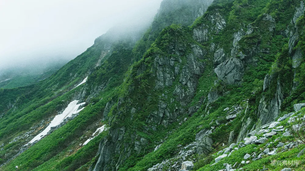 高清摄影  山脚下是一片绿草环绕的山坡，山坡上长满了郁郁葱葱的树木。
