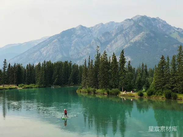 高清摄影 人站在小船上用桨靠近高绿树下的山