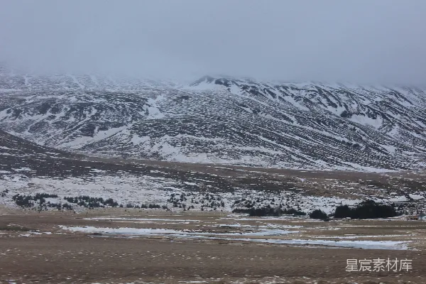 高清摄影 远处一片白雪皑皑的山峦，在 foreground 有一片田野。