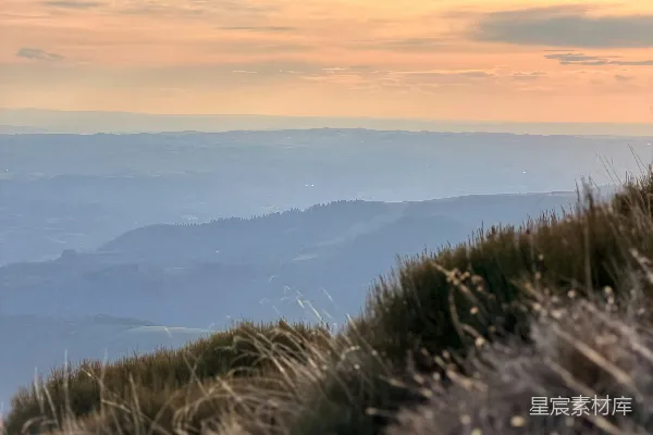 高清摄影 夕阳下的草地山坡与远处的淡薄山峦。