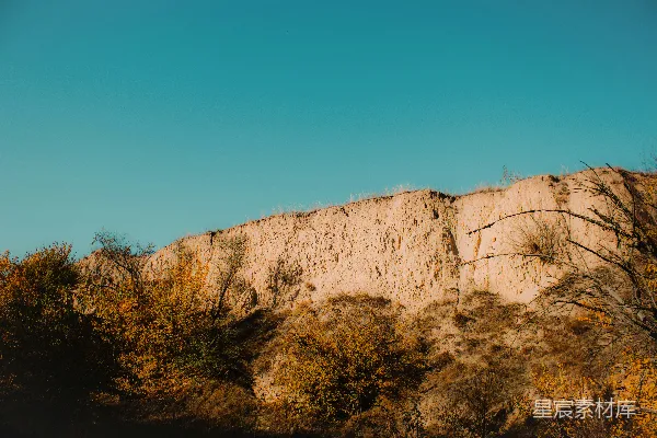 高清摄影 地势险峻的悬崖峭壁下，稀疏的植被在蓝天映衬下显得更加宁静。