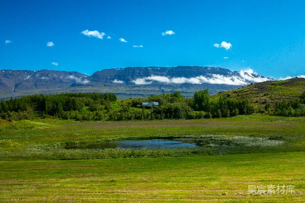 高清摄影 背景中有草地、一个小池塘和远处的山峰。