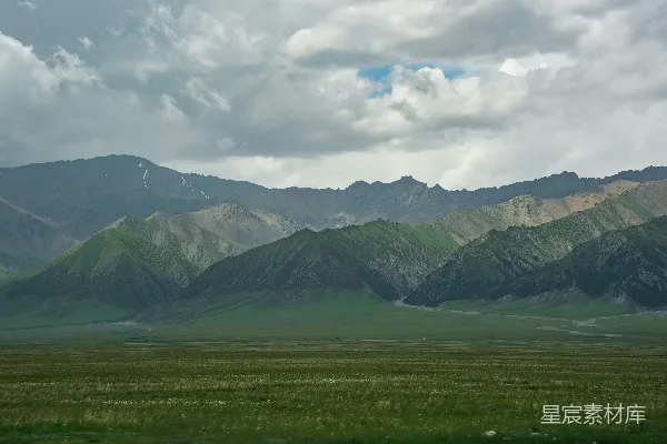 高清摄影 一片广阔翠绿的原野向着山峦延伸，在阴云密布的天空下。