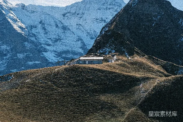 高清摄影 一座建筑坐落在被雪覆盖的山峰下方的草坡上。