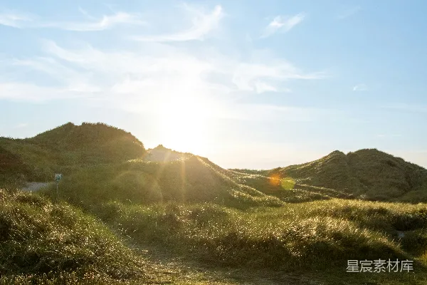 高清摄影 夕阳映照在一片草丛沙丘上，蓝天白云。