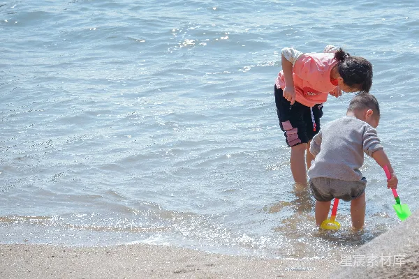 高清摄影 红衣男子抱着一件白上衣的孩子在海滩白天散步