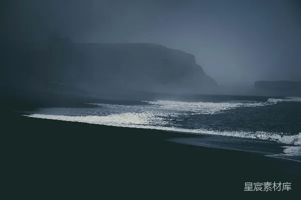 高清摄影 一片有海浪的海滩，背景中有一块大石头。