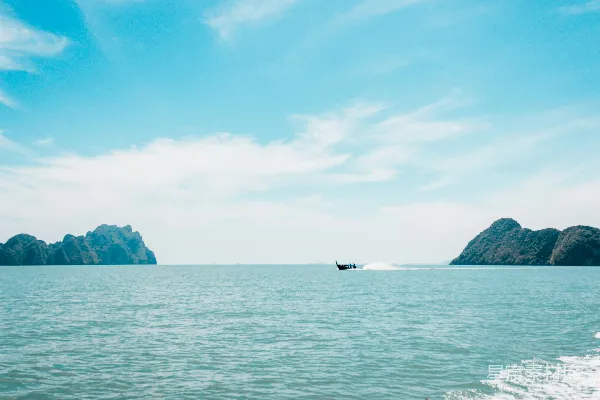高清摄影 白天小船在海中靠近岛屿航行，天空湛蓝。