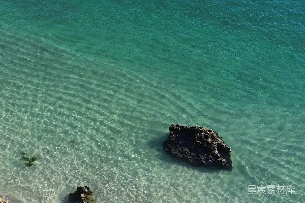 高清摄影 一片沙子覆盖的海滩，清澈湛蓝的海水和岩石。