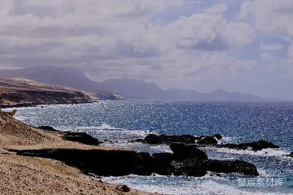 高清摄影 岩石嶙峋的海滩，背景是水面和远处的山脉。