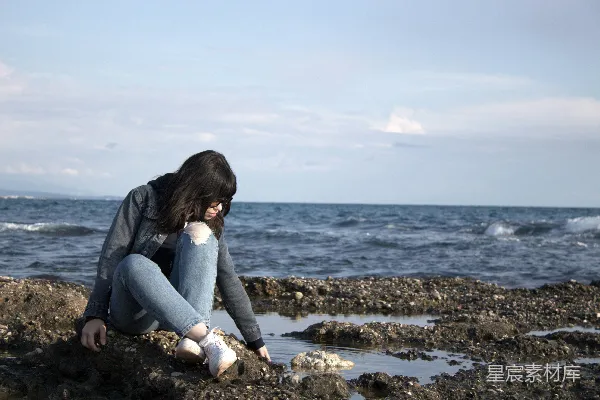 高清摄影 一个女人坐在岩石海滩旁的海边。