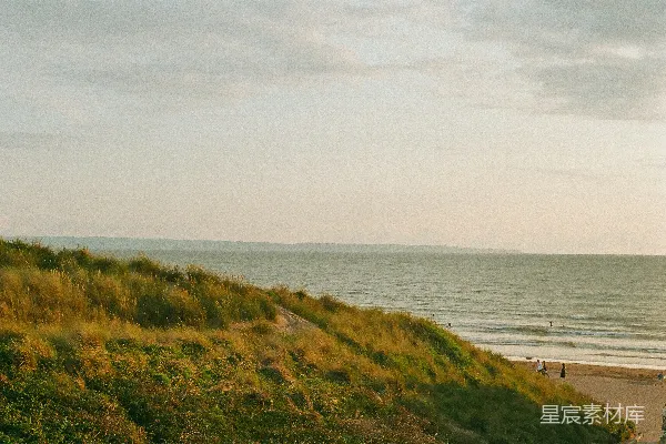 高清摄影 海边一片草地延伸的小山坡上有人行走。