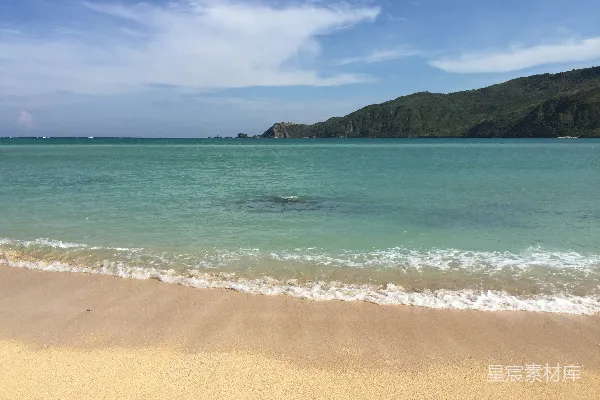 高清摄影 海边有波浪，背景有一座小山。