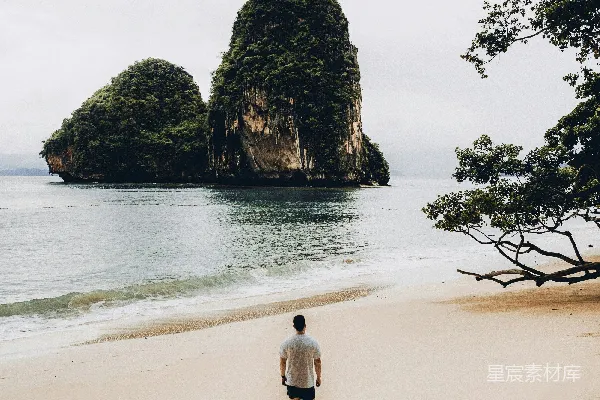 高清摄影 白色T恤的男人在岸边行走，面向两座小岛。