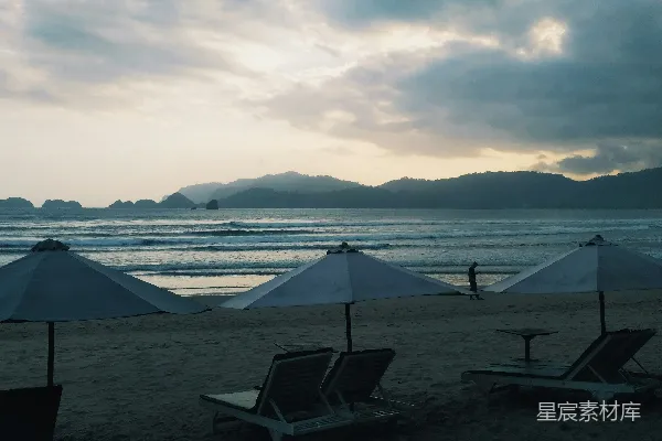 高清摄影 海滩上的躺椅和遮阳伞，背景是山峦。