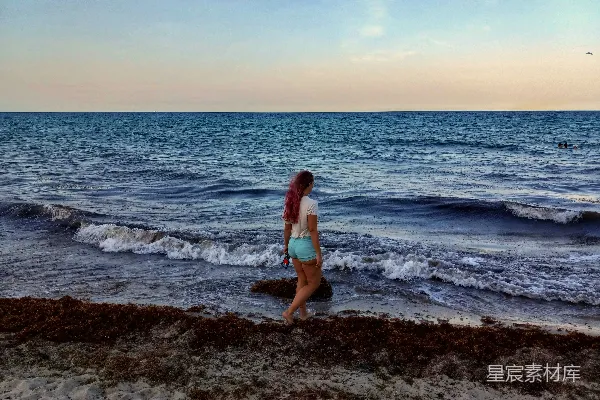 高清摄影 一个女人沿着海滩走，靠近大海。