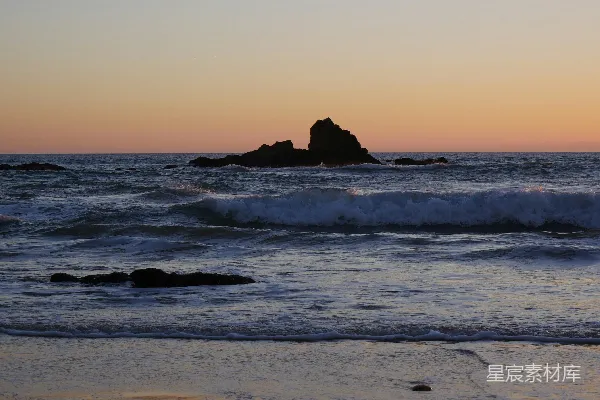 高清摄影 夕阳西下，海面上有一座岩石在远处。