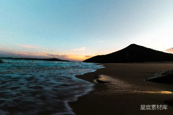 高清摄影 一个有波浪涌来的大海沙滩和远处的山峰。